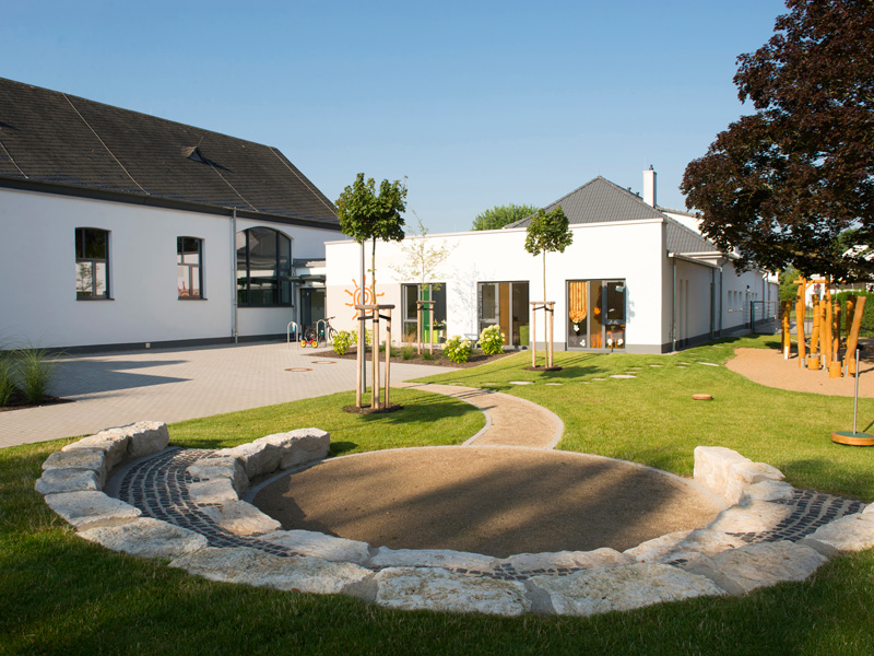 Modernes Kindergartengebäude mit gepflegtem Außenbereich und Spielplatz bei sonnigem Wetter
