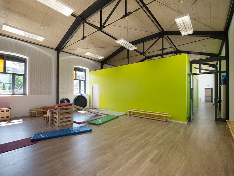 Heller Bewegungsraum im Kindergarten mit Holzboden, grüner Wand und Turngeräten zum Spielen und Klettern