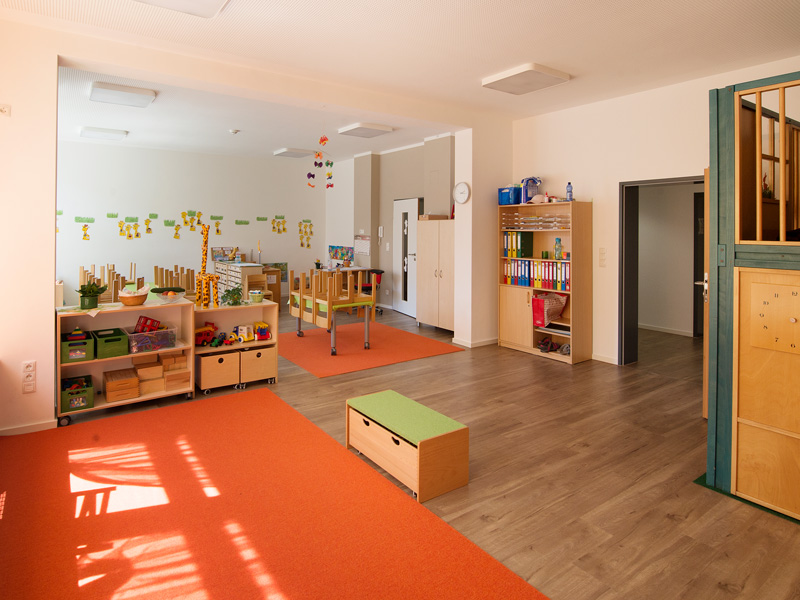 Heller Kindergarten Gruppenraum mit Regalen Spielzeug Holztischen und orangefarbenen Teppichen