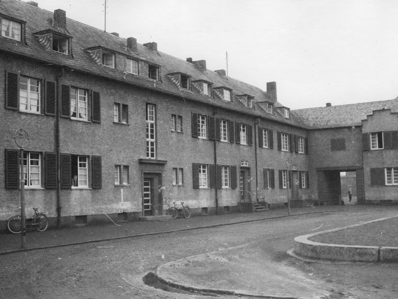 Historisches Schwarz-Weiß-Foto eines Wohngebäudes mit dunklen Fensterläden und Fahrrädern vor der Fassade