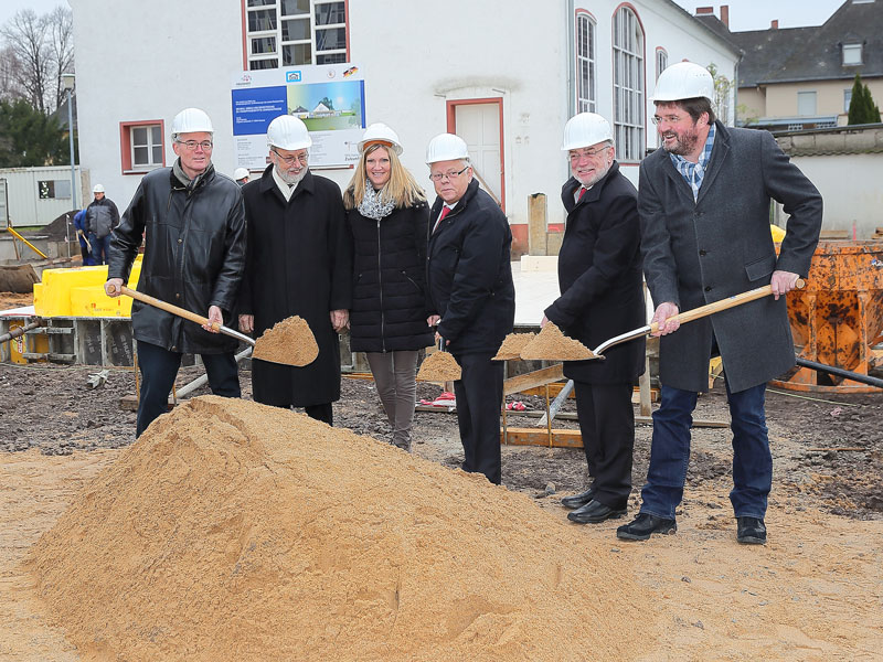 GSG_Chronik_01_800x600px_sRGB Sechs Personen mit Bauhelmen beim feierlichen ersten Spatenstich auf einer Baustelle mit Sandhaufen