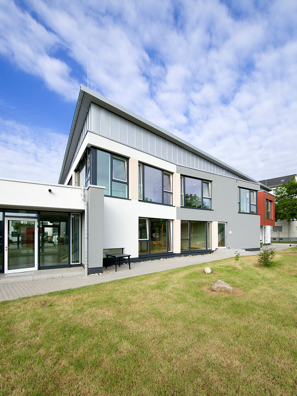 Modernes zweistöckiges Kindergarten Gebäude mit grauer Fassade und großen Fenstern vor einer Rasenfläche