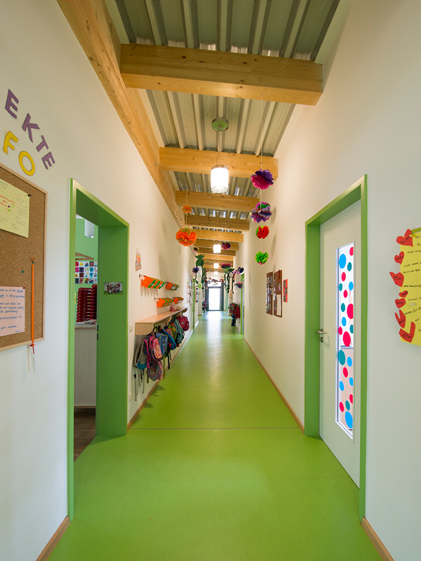 Langer bunter Flur in einem Kindergarten mit grünem Boden, Holzbalkendecke und dekorativen Papierblumen