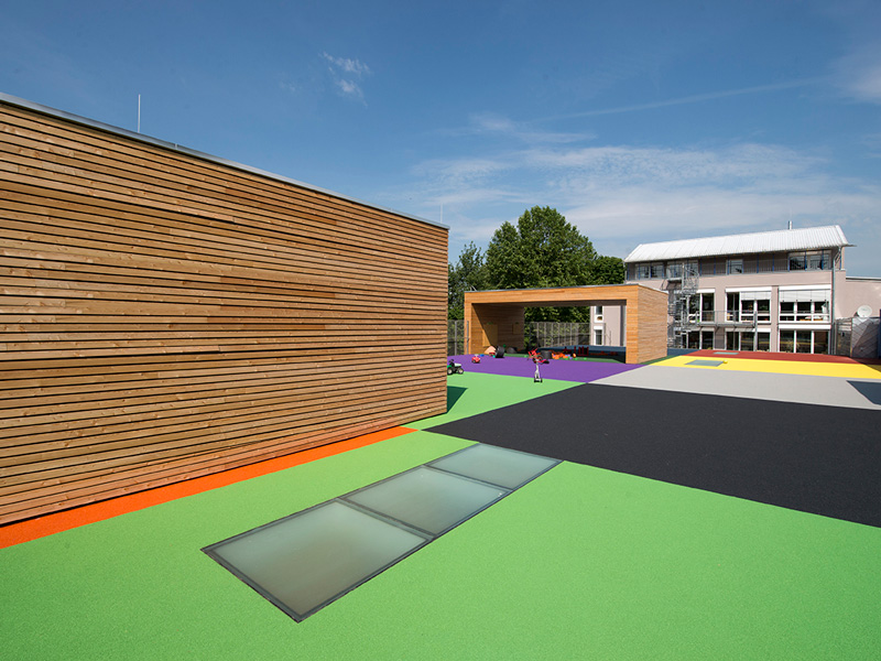 Moderner Kindergarten mit buntem Bodenbelag und hölzernem Spielhaus unter freiem Himmel