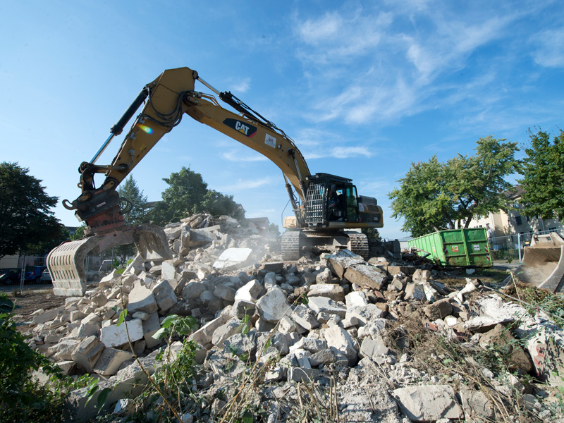 Ein gelber Kettenbagger räumt auf einer Baustelle einen großen Haufen aus Bauschutt und Betonbrocken auf