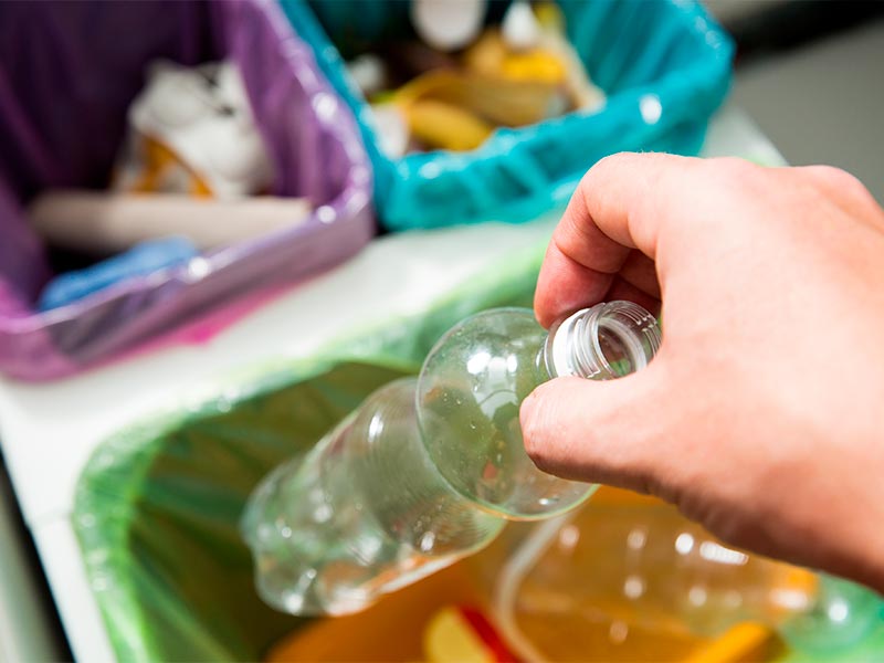 Eine Hand wirft eine leere Plastikflasche in einen Mülltrennung Behälter zur korrekten Abfallentsorgung