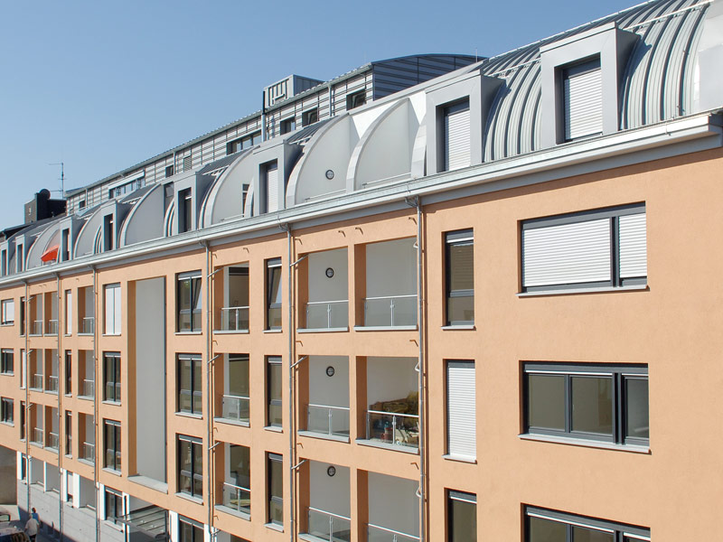 Moderne Fassade eines Wohngebäudes mit Balkonen und gewölbtem Dach bei blauem Himmel