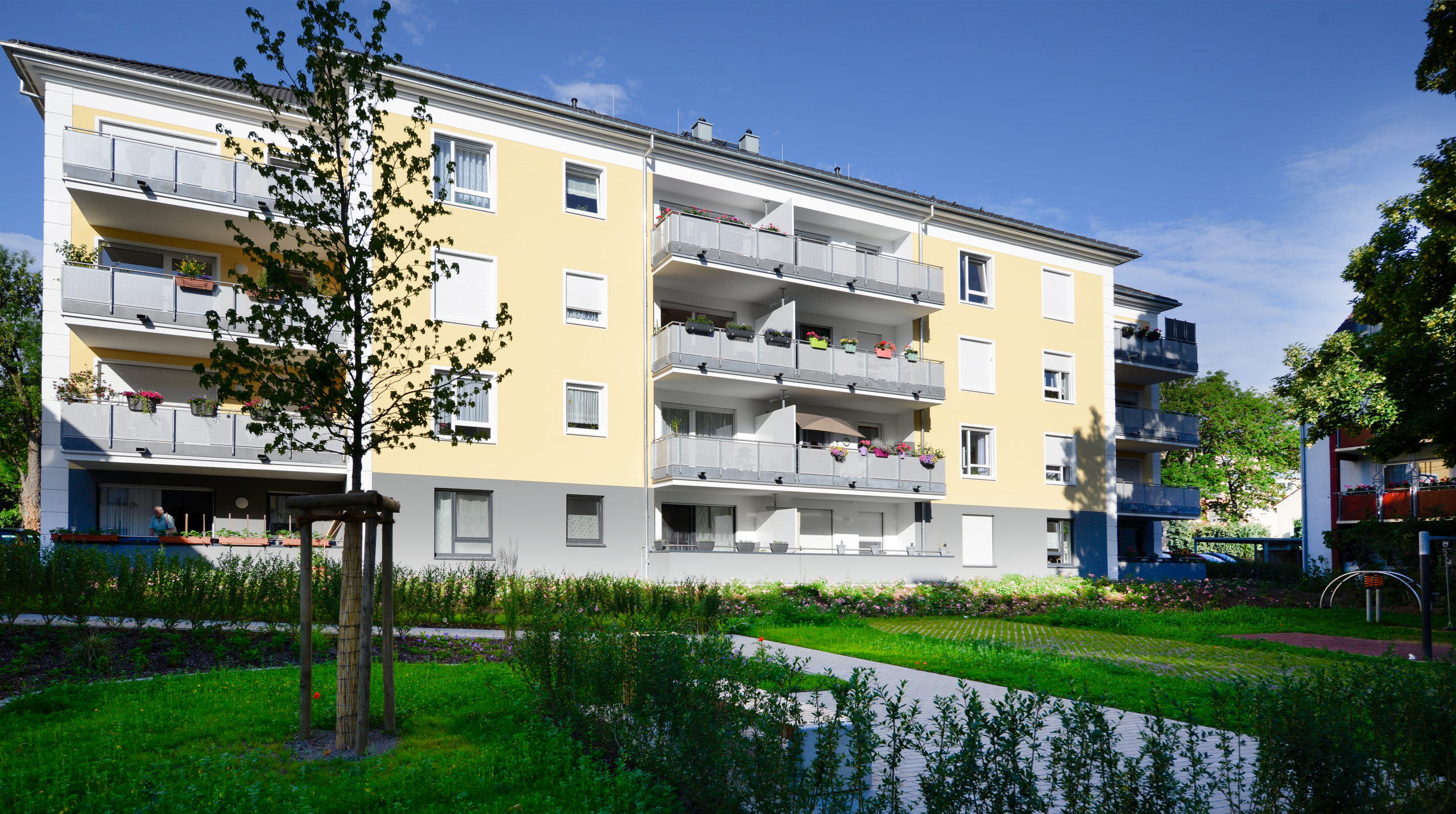 Am-Schloßpark-13 Modernes gelbes Mehrfamilienhaus mit Balkonen und Grünanlage an einem sonnigen Tag