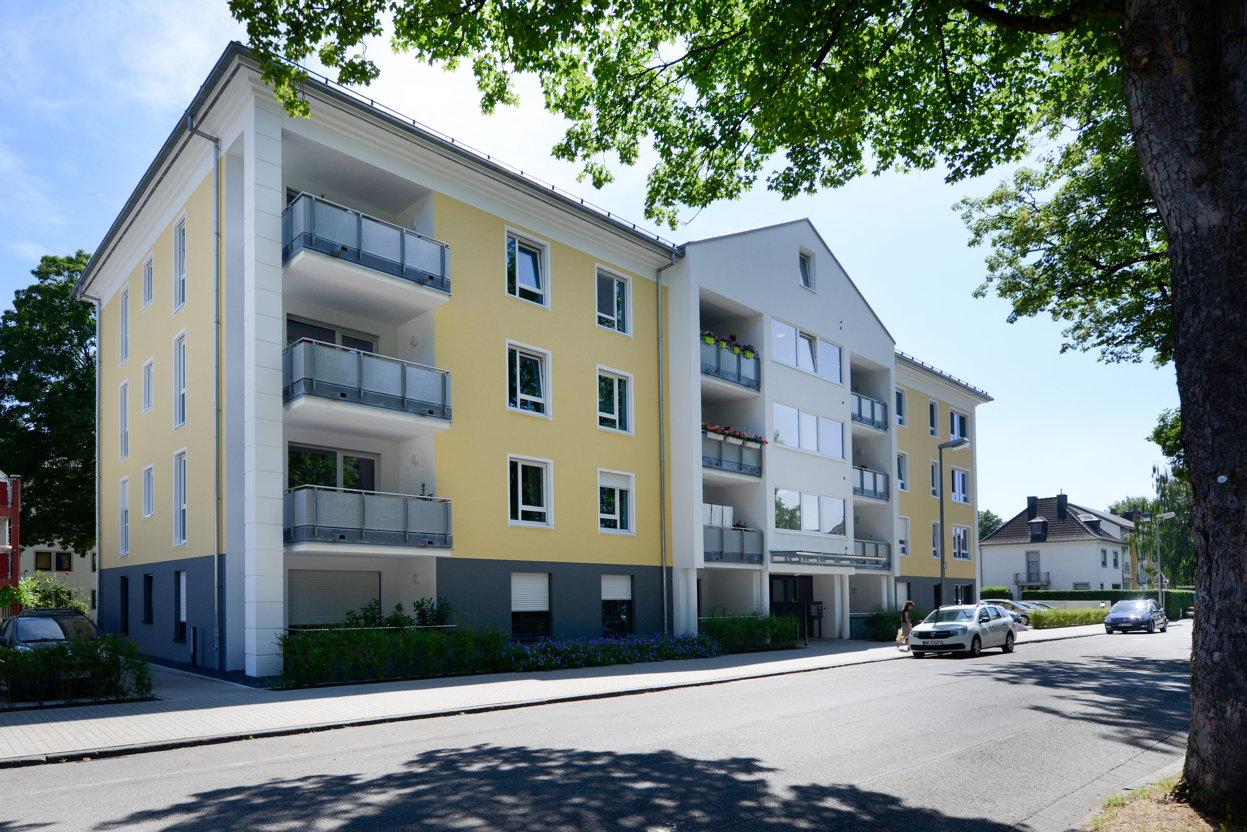 Am-Schloßpark-2 Modernes Mehrfamilienhaus mit gelber Fassade, Balkonen und angrenzender Straße an einem sonnigen Tag
