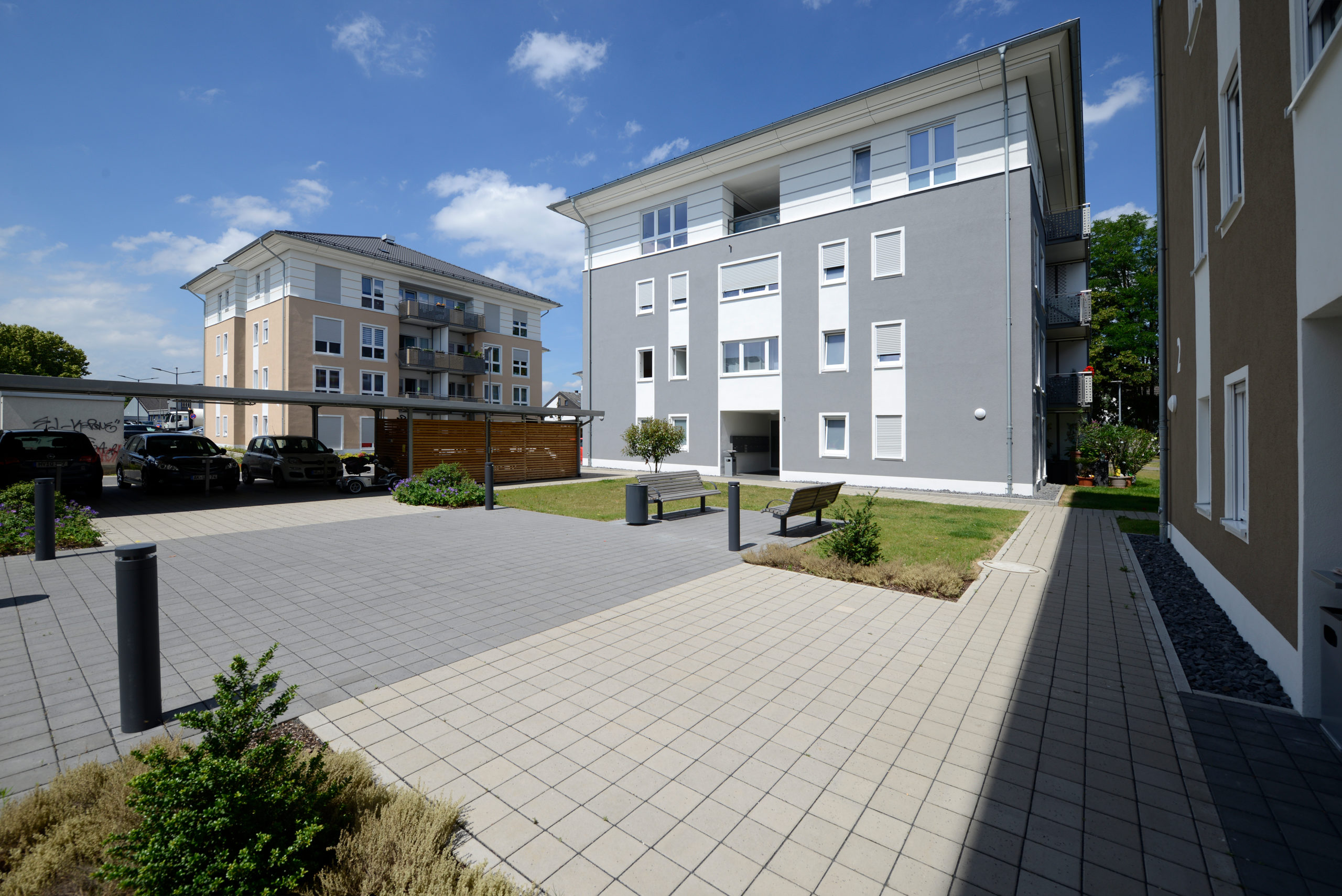 Zeppelinhof-8 Moderne Wohngebäude mit gepflastertem Innenhof, Grünflächen, Sitzbänken und Parkplätzen bei Sonnenschein