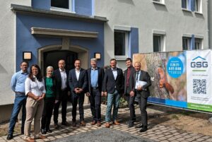 Eine Gruppe von Fachleuten steht vor einem Wohngebäude neben einem Werbebanner der GSG mit Eichhörnchenmotiv