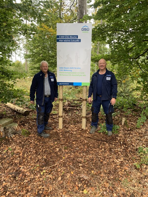 Zwei GSG Mitarbeiter stehen vor einem Hinweisschild zur Wiederaufforstung in einem Wald