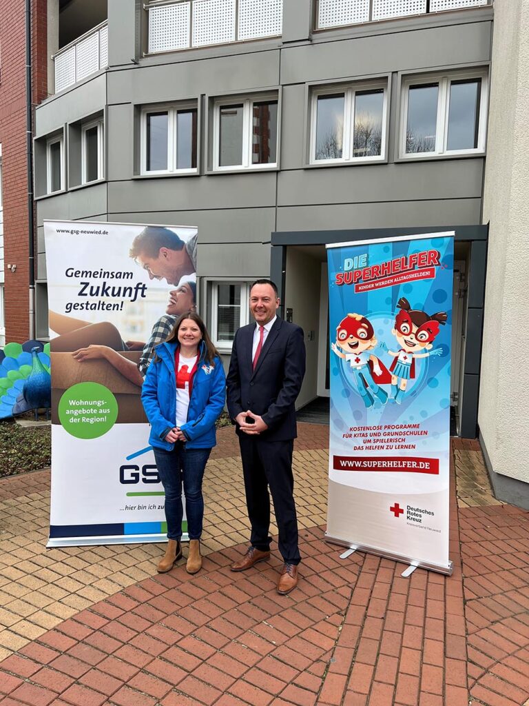 Eine Frau und ein Mann stehen vor zwei Werbeaufstellern für das Superhelfer Projekt des Roten Kreuzes