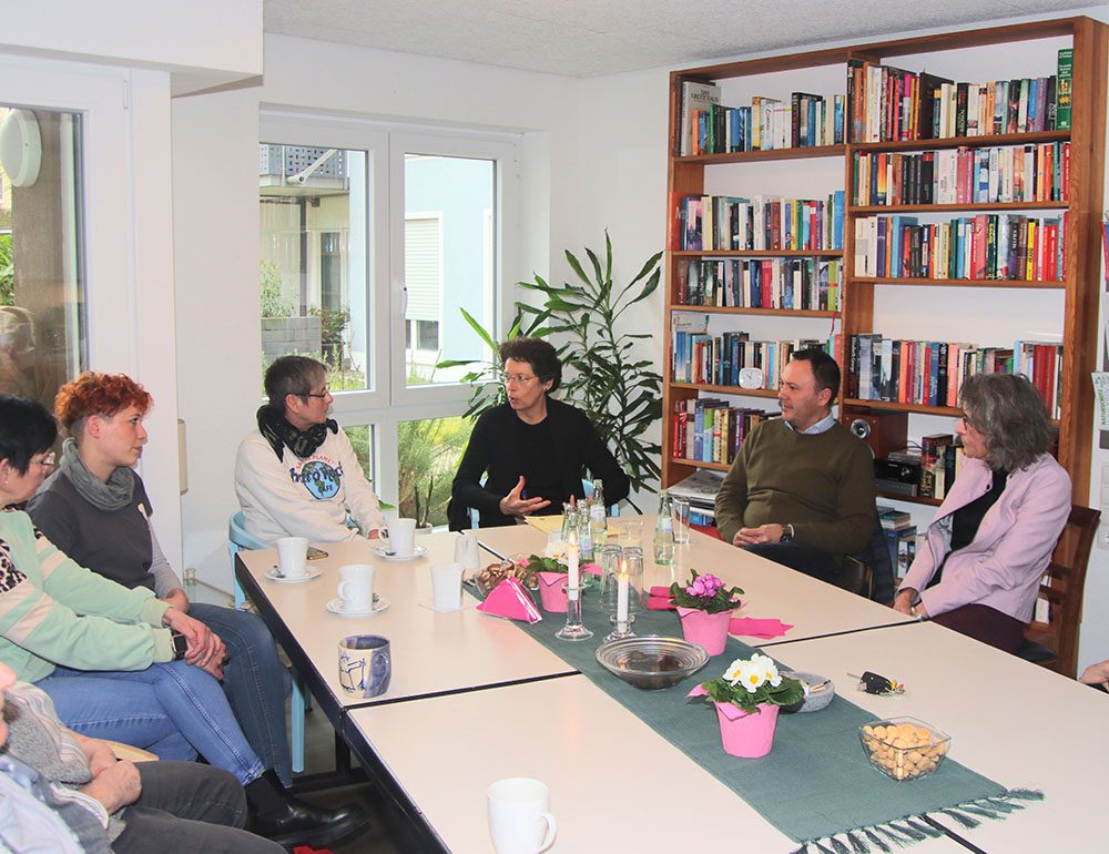 Eine Gruppe von Menschen sitzt interessiert an einem Konferenztisch in einem Raum mit einem großen Bücherregal