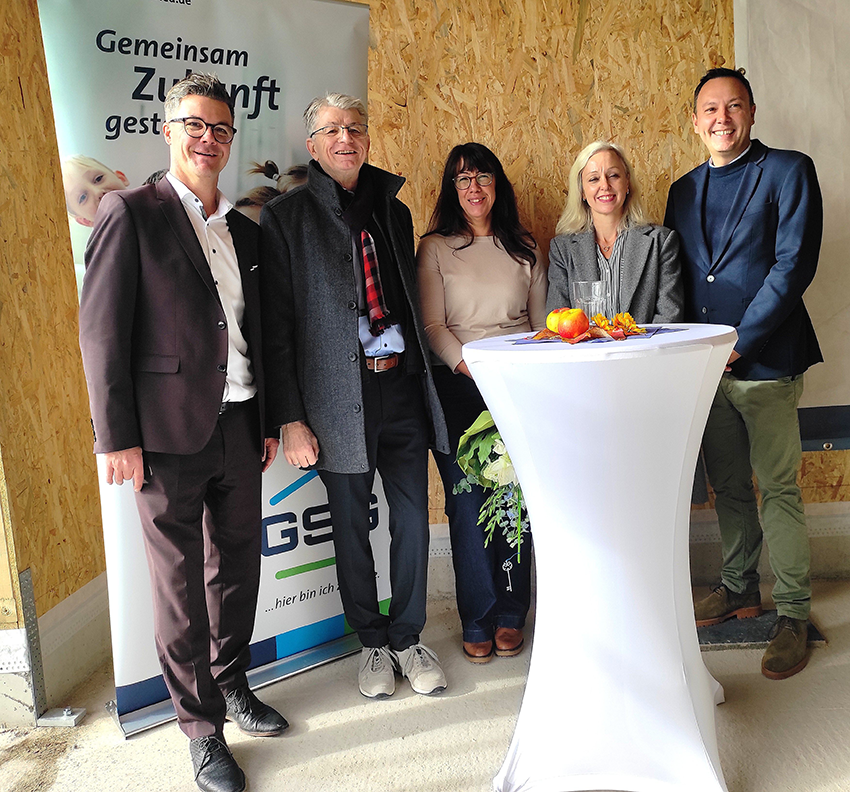 Gruppe von Menschen beim Richtfest vor einem GSG Banner an einem Stehtisch mit Blumenstrauß