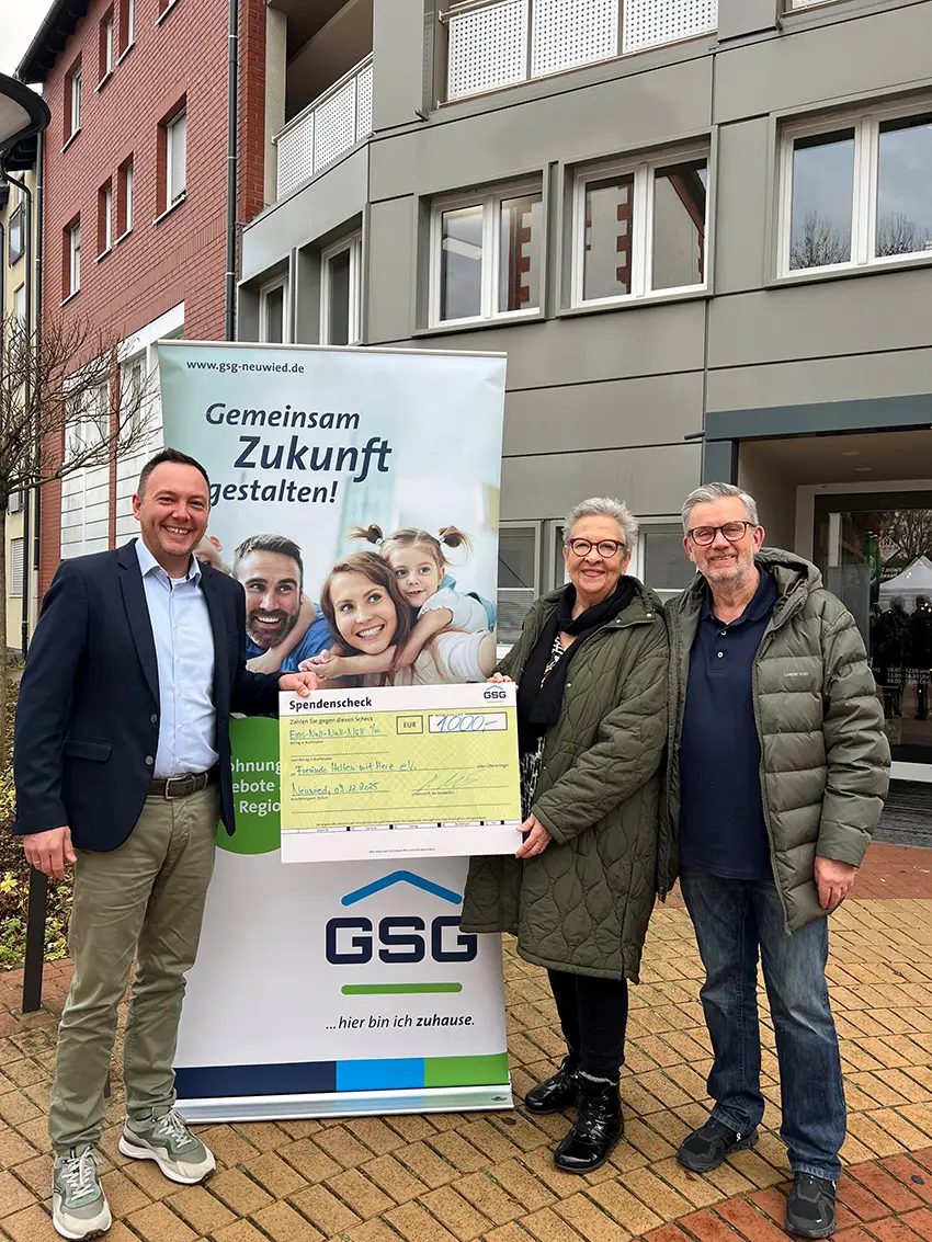 Drei Personen halten gemeinsam einen Spendenscheck vor einem GSG Werbebanner im Freien