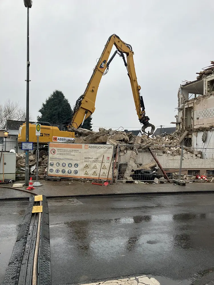 Gelber Bagger bei Abrissarbeiten eines Gebäudes hinter einem Bauzaun