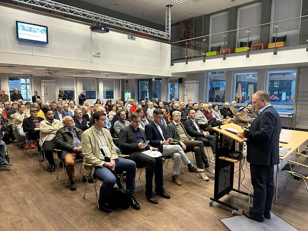 Ein Redner spricht bei einer Informationsveranstaltung vor einem aufmerksamen Publikum in einem modernen Konferenzraum