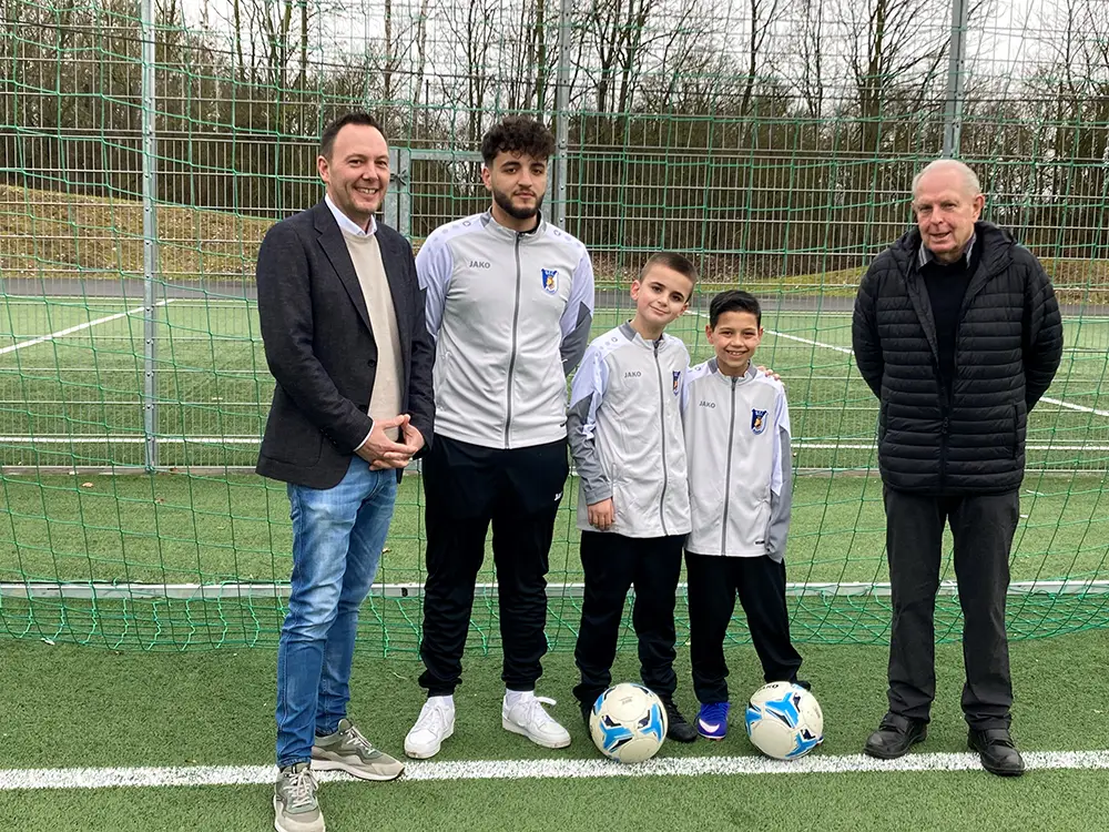 Zwei Erwachsene und zwei Kinder in Sportkleidung mit Fussbällen auf einem Sportplatz bei der Fotoübergabe