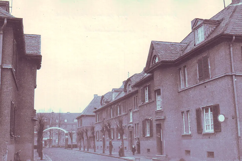 GSG-100-Jahre-Vorzeige-Siedlung Historische Ansicht einer Wohnsiedlung mit Backsteinhäusern und Bäumen entlang einer ruhigen Straße
