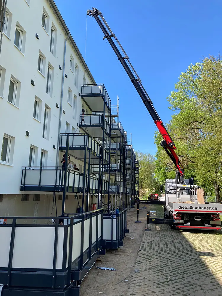 Installation-der-Balkone Ein Baukran montiert neue Balkone an der Fassade eines Wohnhauses während der Modernisierung