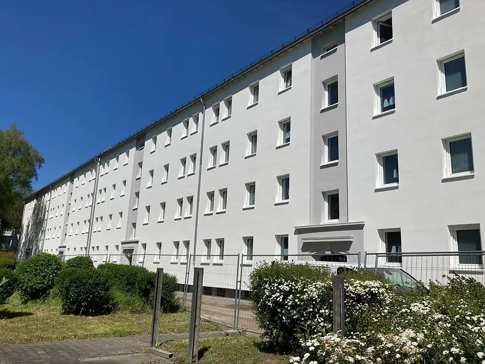 Modernisiertes helles Wohngebäude mit vielen Fenstern vor blauem Himmel und Gruenanlagen