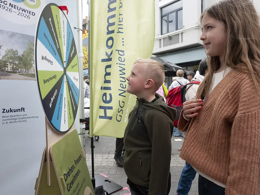 R_Claassen-1044649 Zwei Kinder betrachten gespannt ein buntes Glücksrad an einem Informationsstand bei einer Outdoor-Veranstaltung