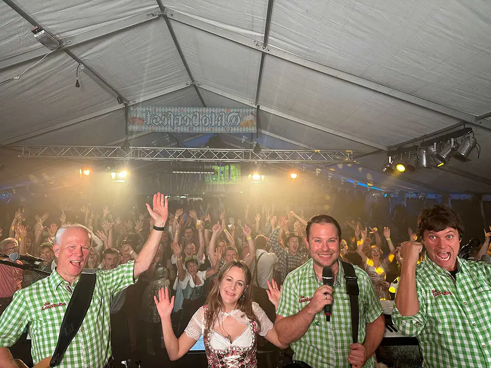 Die Musikband Die Lausbuba spielt in Trachten auf einer Festbühne vor einem jubelnden Publikum im Festzelt