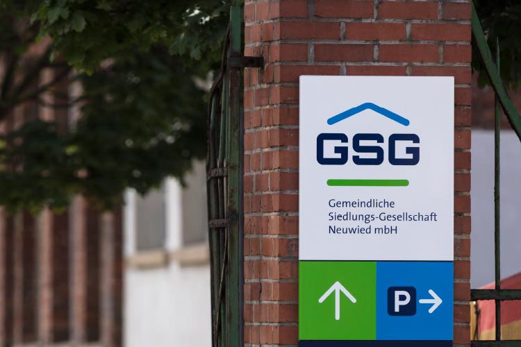 Weißes Unternehmensschild der GSG mit Firmenlogo und Parkplatzpfeilen an einem massiven Backsteinpfeiler befestigt