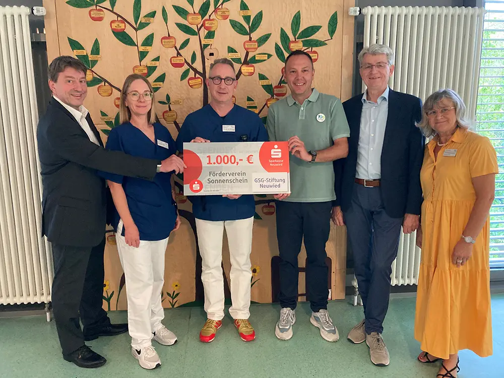Eine Gruppe von Menschen hält gemeinsam einen symbolischen Spendenscheck über 1000 Euro für den Förderverein Sonnenschein