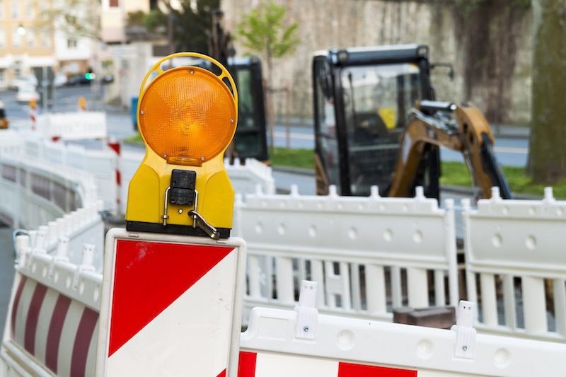 Baustelle mit gelber Warnleuchte auf einer Leitbake und einem Bagger bei einer halbseitigen Straßensperrung