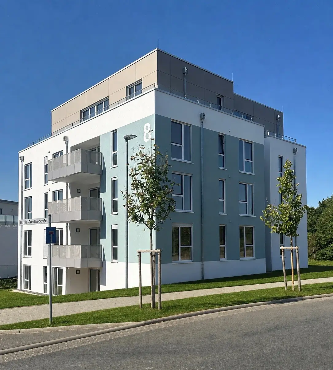 Mehrfamilienhaus mit blaugrüner Fassade und Balkonen an einer ruhigen Straße bei strahlend blauem Himmel