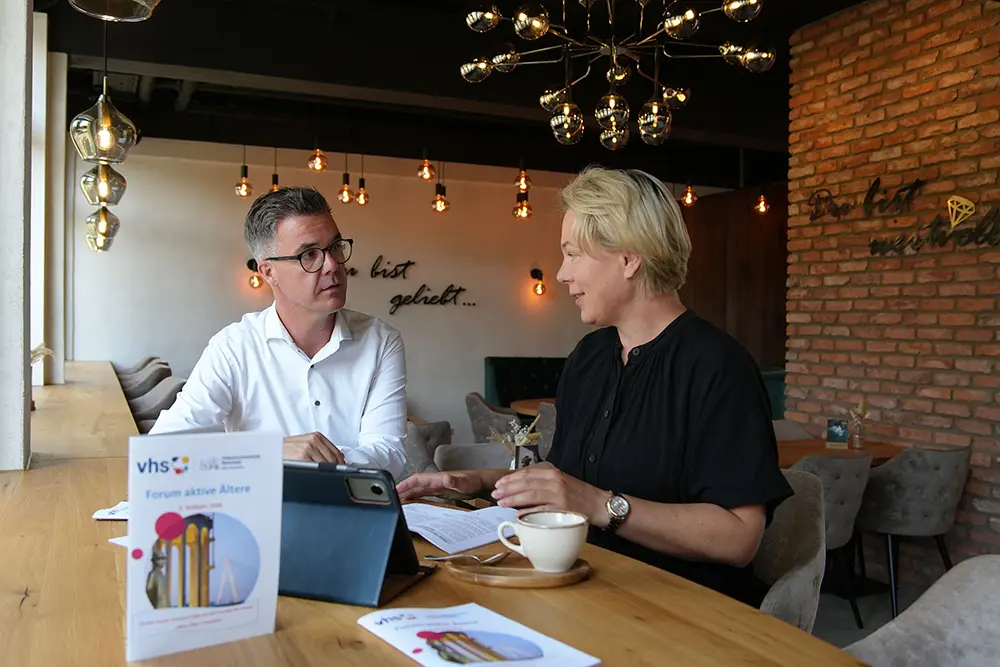 Peter Jung und Yuliya Meissner im Gespraech an einem Tisch mit Unterlagen zum Forum Aktive Aeltere