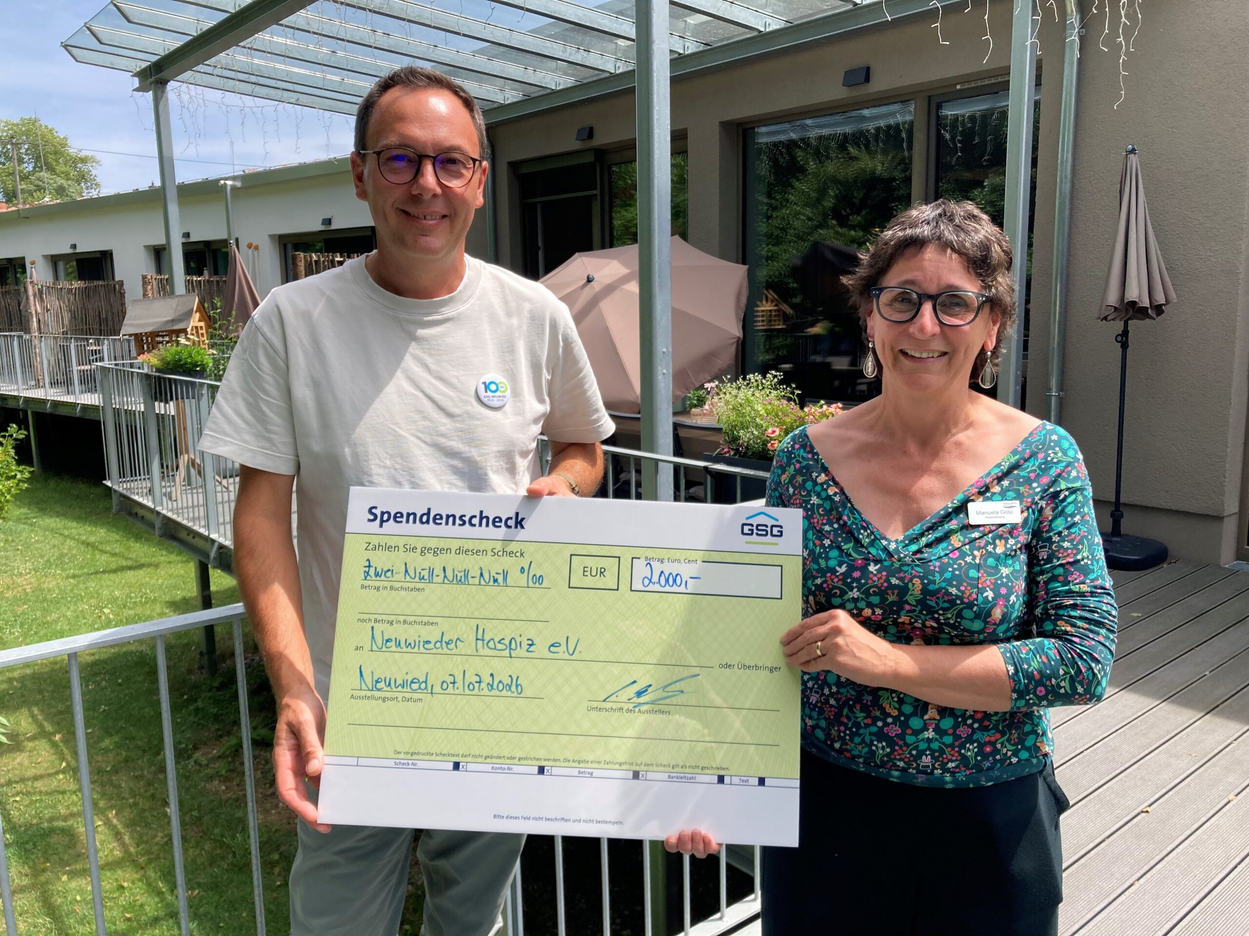 Ein Mann und eine Frau halten gemeinsam einen symbolischen Spendenscheck über 2000 Euro für das Hospiz in die Kamera