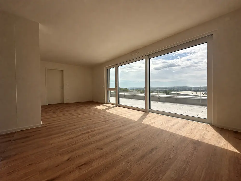Lichtdurchfluteter Wohnraum einer Neubauwohnung mit Holzboden und bodentiefen Fenstern zu einer großen Dachterrasse