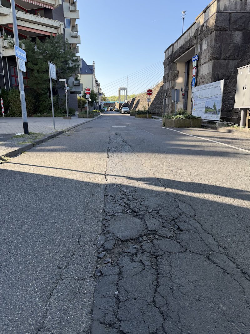 Sanierungsbedürftige Deichstraße mit Straßenschäden und Hinweisschildern zur geplanten Erneuerung