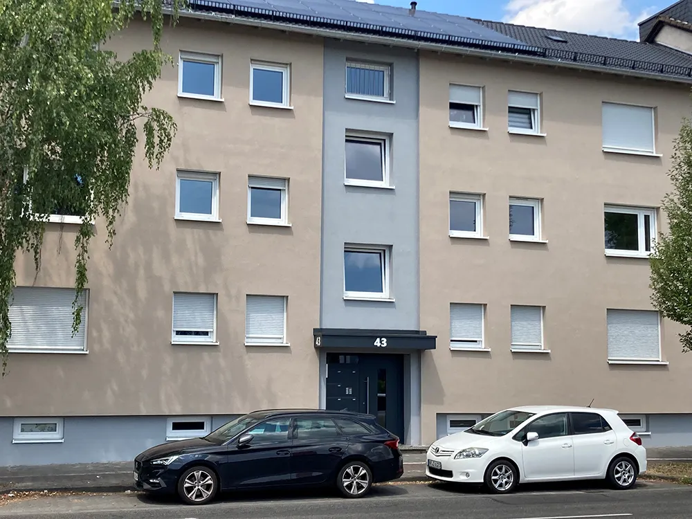 Modernisiertes GSG-Wohnhaus der 60er-Jahre mit beiger Fassade, grauem Treppenhaus und zwei Autos davor
