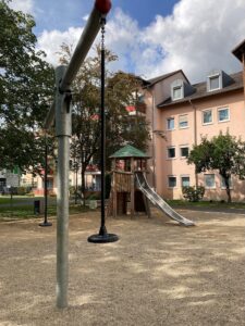 Kinderspielplatz der GSG im Grünen mit Holzspielgerät, Rutsche und Schaukel vor Wohngebäuden.