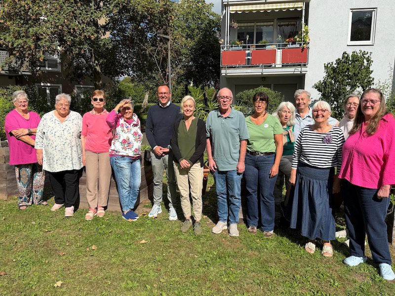 Gruppe lächelnder Menschen der GSG-Geschäftsführung beim Gedankenaustausch im Grünen vor einem Wohngebäude